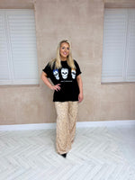 Model wearing a black oversized t-shirt with a three coloured graphic skull styled with gold sequin trousers